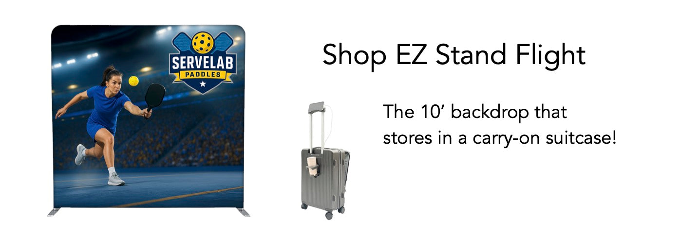 A promotional banner for an EZ Stand flight-sized backdrop, showing a printed tennis-themed backdrop stand on the left and a gray carry-on suitcase on the right with text reading 'Shop EZ Stand Flight' and 'The 10' backdrop that stores in a carry-on suitcase!'.