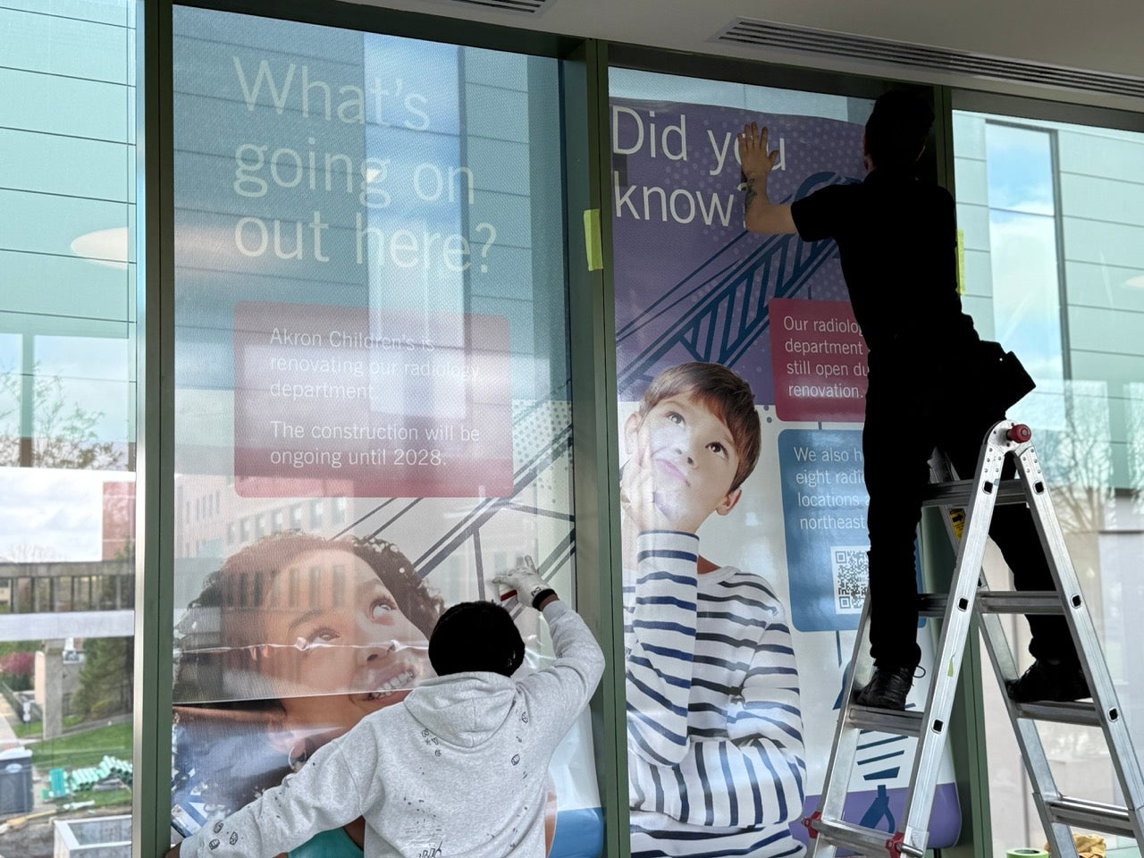 DG Creativ Installers applying window perf graphics with an optically clear over laminate on one of Akron Children's Hospital pedestrian bridges